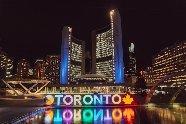 Illuminated Toronto sign at night, city lights background.